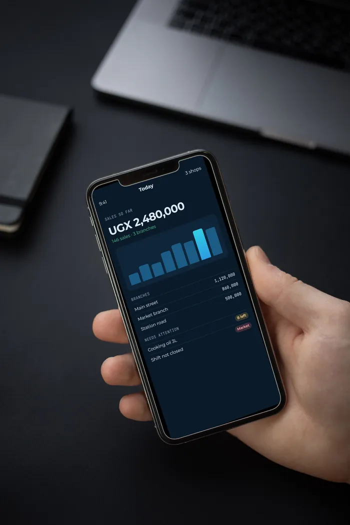 A hand holding a phone showing a shop owner's daily sales with sample data.